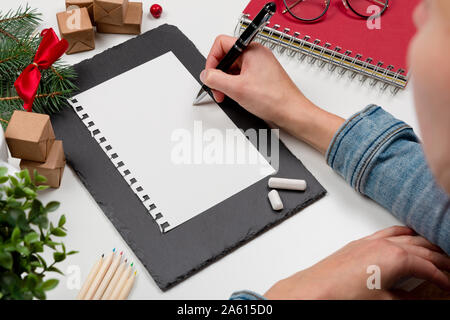 Christmas letter writing on paper on white desk with decorations. Wish list writing. 2020 resolution list Stock Photo