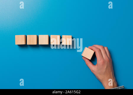 Woman's hand establishes a wooden cubes in row. Blank wooden blocks for word, text or illustration. Hand placing cube and finishing the row Stock Photo