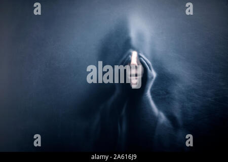 Ghostly figure behind a dusty scratched glass. Scary figure with part of mannequin head in hands Stock Photo