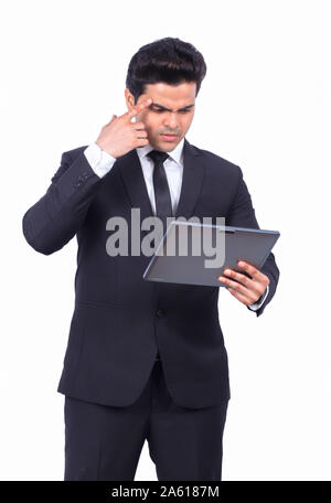 Serious young businessman using digital tablet. Confused male professional is holding wireless computer. He is wearing formals on white background. Stock Photo