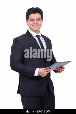 Portrait of handsome young businessman using digital tablet. Confident male professional is smiling. He is wearing suit on white background. Stock Photo