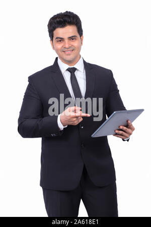 Handsome young businessman pointing at digital tablet. Male professional is preparing presentation on wireless computer. He is wearing suit on white b Stock Photo