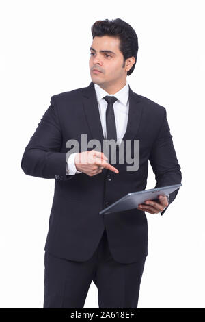 Serious young businessman pointing at digital tablet. Male professional is preparing presentation on wireless computer. He is wearing suit on white ba Stock Photo
