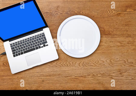 Modern laptop and empty plate on textured wooden table view from above Stock Photo