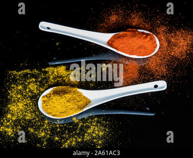 Elegant composition of two white ceramic spoons filled with colorful spices against a shiny black reflective background Stock Photo