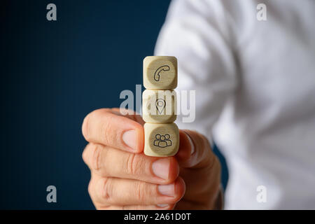 Businessman holding three stacked wooden dices with contact and information icons on them. Stock Photo