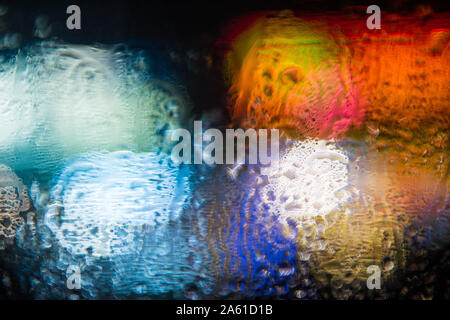 abstract out of focus bold coloured lights shot on the street rain on a car window, high quality good for backgrounds and eye catching advertising. Stock Photo