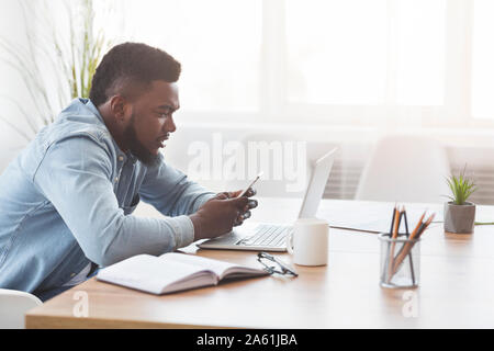 Black office worker using smartphone at workplace Stock Photo