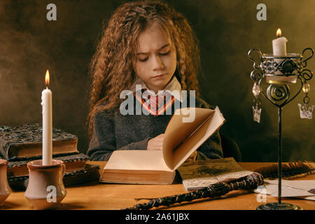 Portrait of a pretty enchantress child with magnificent long brown hair dressed in a navy blue jumper, white shirt and red tie. She is reading a book Stock Photo