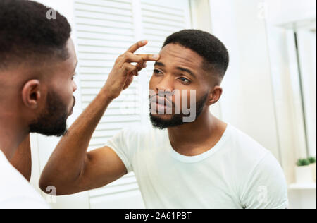 Young worried african man checking his wrinkles Stock Photo