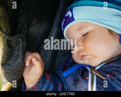 tired baby sleeping in a stroller. Cute adorable caucasian blond toddler bou sleeping in stroller at daytime. Children healthcare and happy childhood Stock Photo