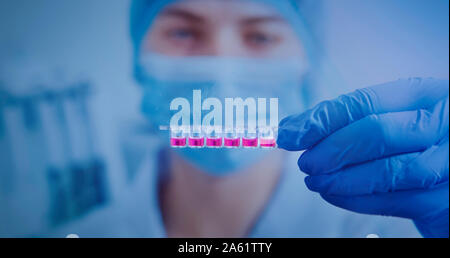 Laboratory assistant in mask and gloves analyzing pink liquid Stock Photo