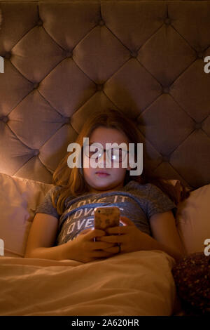Young girl sat in bed watching her cell phone before bed time Stock Photo