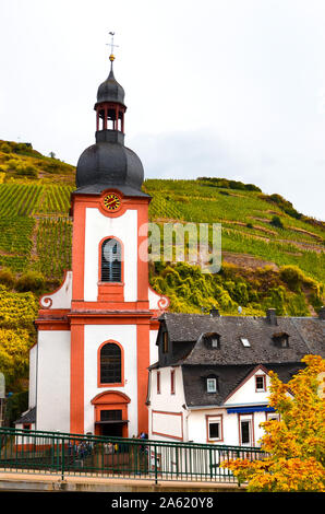 Roman Catholic Church in Zell, Germany. Picturesque village in famous Mosel wine region in the fall season. Autumn vineyards and trees on the slope in the background. German autumn landscapes. Stock Photo