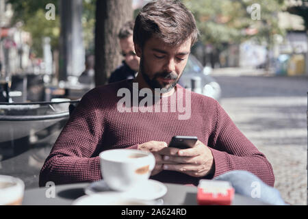 Attractive young bearded man using his smartphone in the cafe Stock Photo