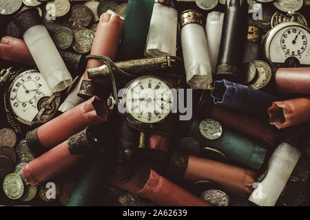 A disordered pile of old objects on the desk, hunting cartridges used, broken pocket watches, old coins, old banknotes and little chains Stock Photo