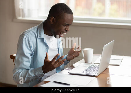 Stressed millennial african ethnic guy irritated by broken computer. Stock Photo