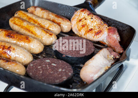 Cumberland sausages, back bacon and black pudding cooking in a griddle pan Stock Photo