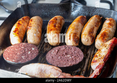 Cumberland sausages, back bacon and black pudding cooking in a griddle pan Stock Photo