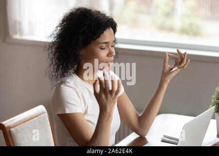 Mindful african ethnicity woman freelancer relaxing with closed eyes. Stock Photo