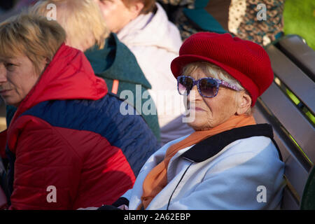 Kharkiv, Ukraine - October 14, 2019: Elegant elderly lady in a red beret resting on a bench in a city park Stock Photo