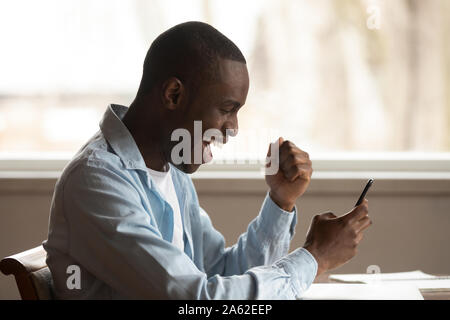 Excited lucky mixed race young man received win sms notification. Stock Photo