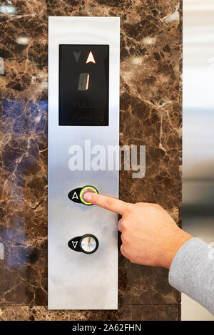 Call the elevator. A man calls a lift with his finger for a ride up, the digging is lit in green. Hand and panel closeup. Stock Photo
