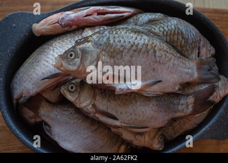 Crucian fish river fish in a round aluminum bowl on a wooden table. Crucian fish in a bowl. Crucian fish sprinkled with seasonings and salt is ready f Stock Photo