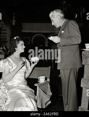 Myrna Loy with Director John Stahl, eating cake on the set of the film ''Parnell' (1937) MGM  File Reference # 33848-910THA Stock Photo