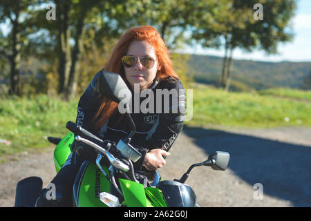 Jawor, POLAND - JUNE 2018 Red-haired girl in sunglasses is sitting on a sports motorcycle. Woman, attractive motorcyclist dressed in motorcycle outfit Stock Photo