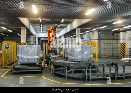 Robot Hand manipulator packaging factory products from conveyor into container. Stock Photo