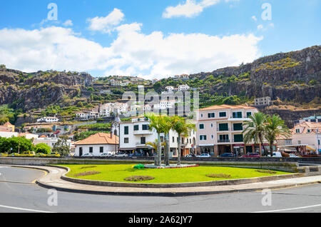 Ribeira Brava, Madeira, Portugal - Sep 9, 2019: Picturesque village with palm trees by the road. Houses on the hill in the background. Green trees and banana plantation among the buildings. Stock Photo