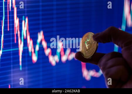 hand holding bitcoin shiner on blurry dark blue exchange chart close-up with selective focus Stock Photo