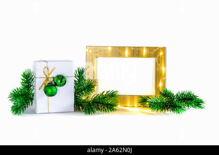Christmas composition: stylish white Christmas present box decorated with golden lace and green Christmas baubles, golden frame with sparkling lights Stock Photo
