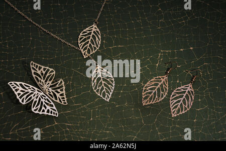 inspired by nature golden leaves and butterfly set necklace and earrings on cracked green background Stock Photo
