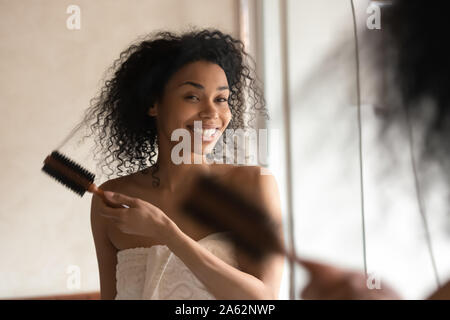 African ethnicity millennial woman brushing, styling, combing curly hair. Stock Photo