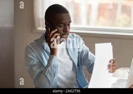 Focused young black man holding documents, calling to financial advisor. Stock Photo