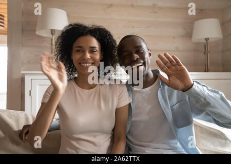 Happy african american family couple waving, sitting on sofa. Stock Photo