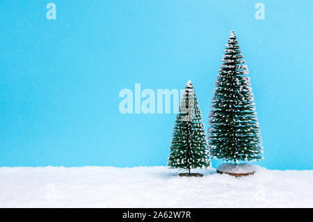 Winter landscape theme with two small Christmas trees on snow against blue paper background. Christmas holiday and winter concept. Copy-space for text Stock Photo