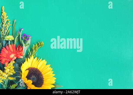 Corner border of different fresh bright colorful summer flowers lying on trendy mint background. Flet lay style. Copy space. Stock Photo