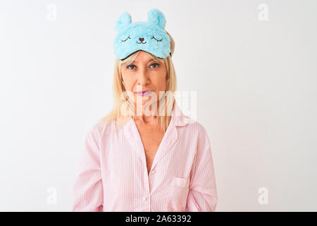 Middle age woman wearing blue sleep mask and pajama over isolated white background with serious expression on face. Simple and natural looking at the Stock Photo
