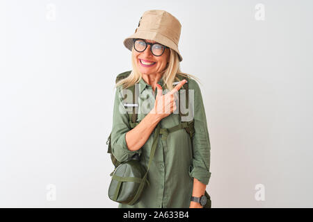 Middle age hiker woman wearing backpack hat canteen glasses over isolated white background cheerful with a smile of face pointing with hand and finger Stock Photo