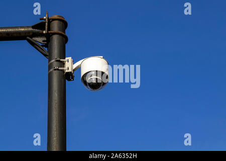White street camera of external supervision installed on an outdoors pole against a blue sky. Modern CCTV camera, surveillance and monitoring. Copy sp Stock Photo