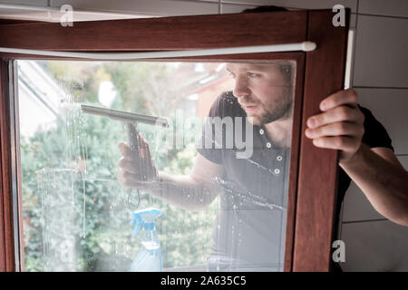 man washes a window in a house using scraper Stock Photo