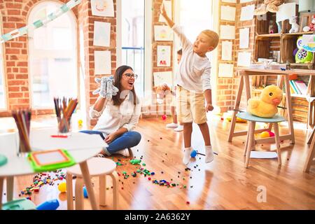 Beautiful teacher and toddlers playing around lots of toys at kindergarten Stock Photo