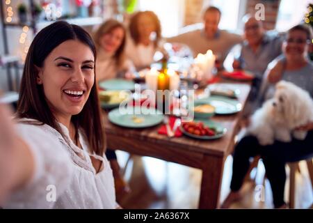 Family and friends dining at home celebrating christmas eve with traditional food and decoration, taking a selfie picture together Stock Photo
