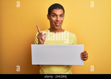 Young handsome arab man holding banner standing over isolated yellow background surprised with an idea or question pointing finger with happy face, nu Stock Photo