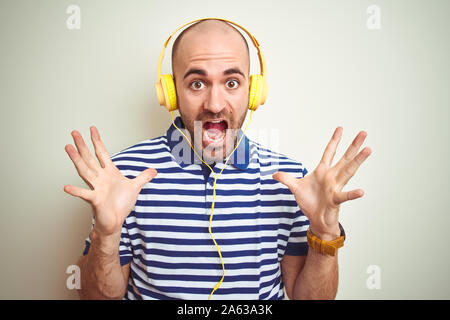 Young man listening to music wearing yellow headphones over isolated background celebrating crazy and amazed for success with arms raised and open eye Stock Photo