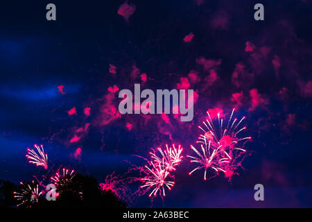 Inexpensive fireworks, over the city sky, red and pink with smoke. For any purpose use. Stock Photo