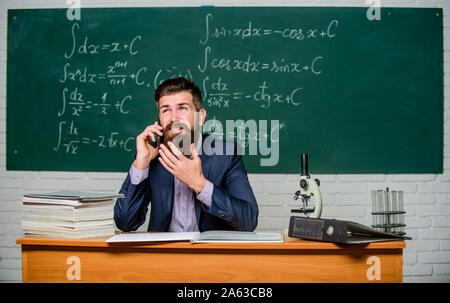 Calling parents. School teacher call mobile phone while sit classroom chalkboard background. Teacher bearded man talk mobile phone. Call colleague ask advice. Pedagogue keep in touch with colleagues. Stock Photo